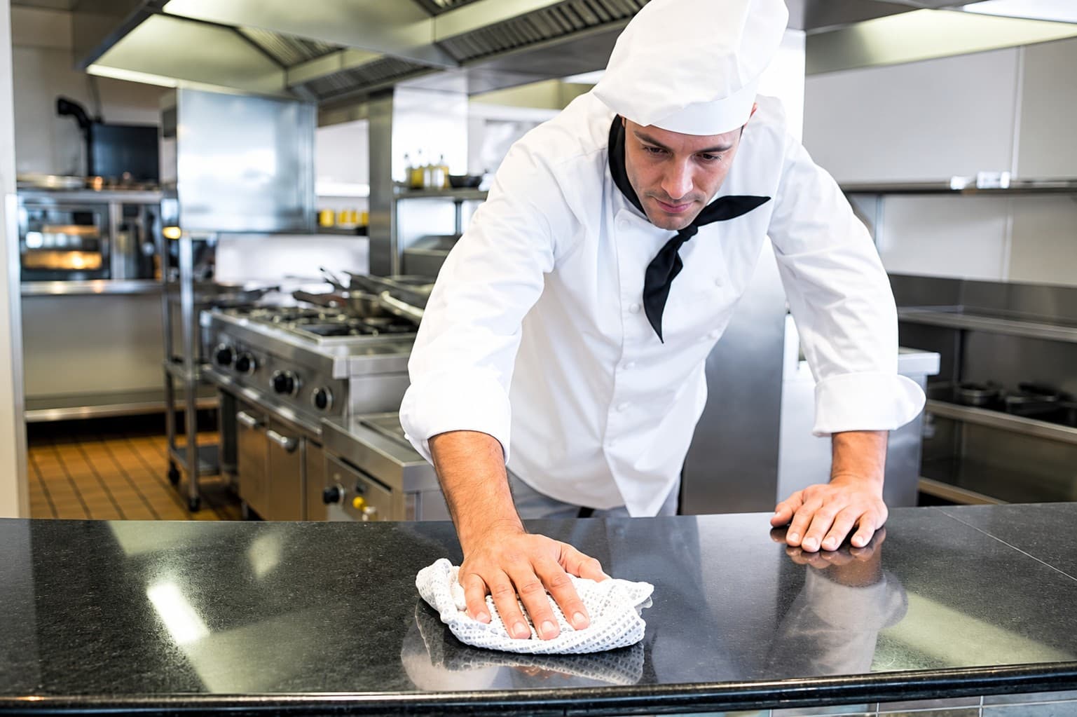 Cocinero limpiando la encimera de una cocina profesional.